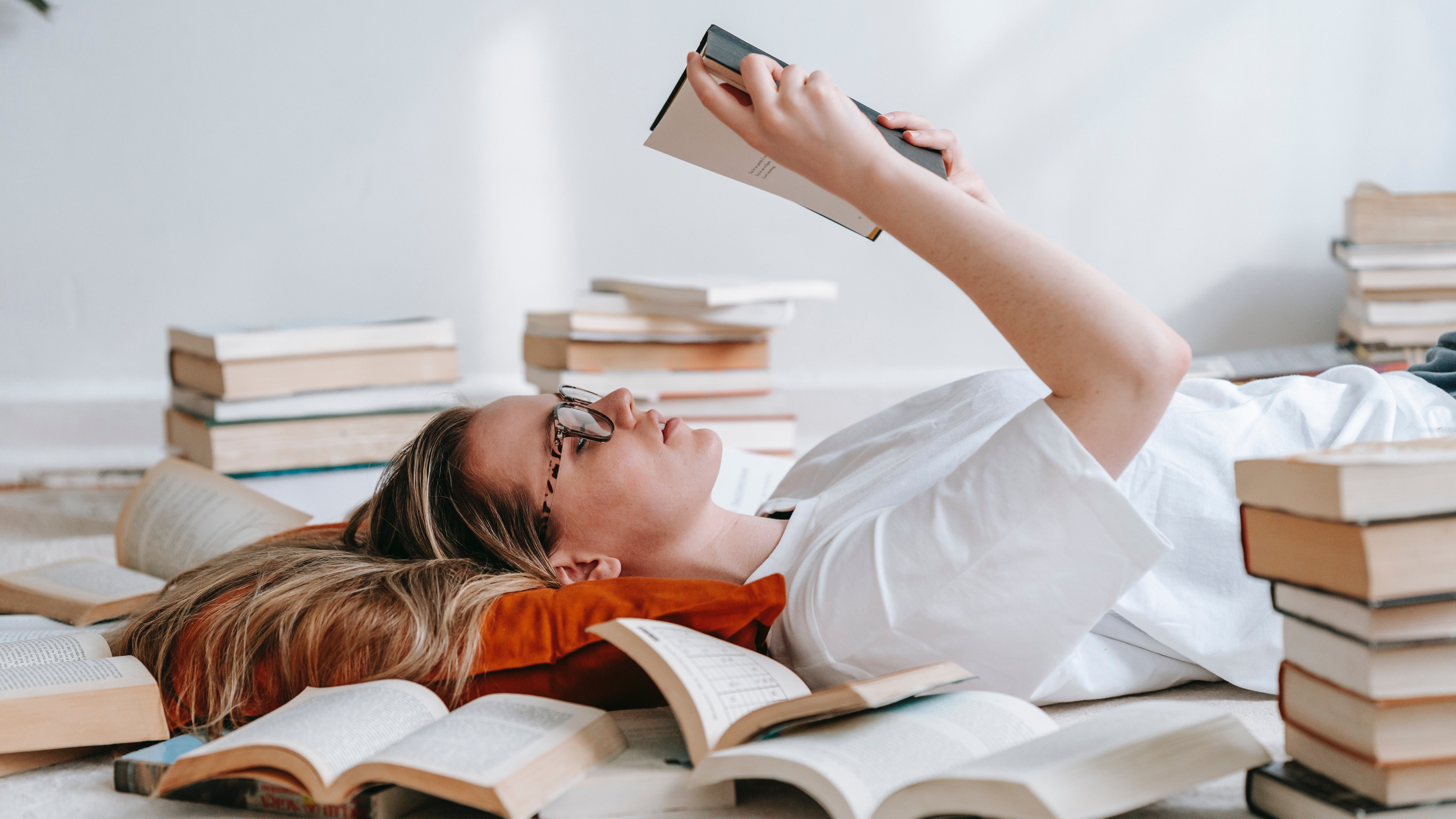 Fiatal nő olvas könyvek között feküdve