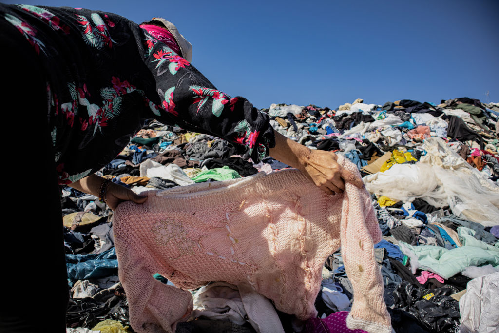 Egy nő keresgél egy szeméttelepen egy hegynyi használt ruha között az Atacama-sivatagban.
