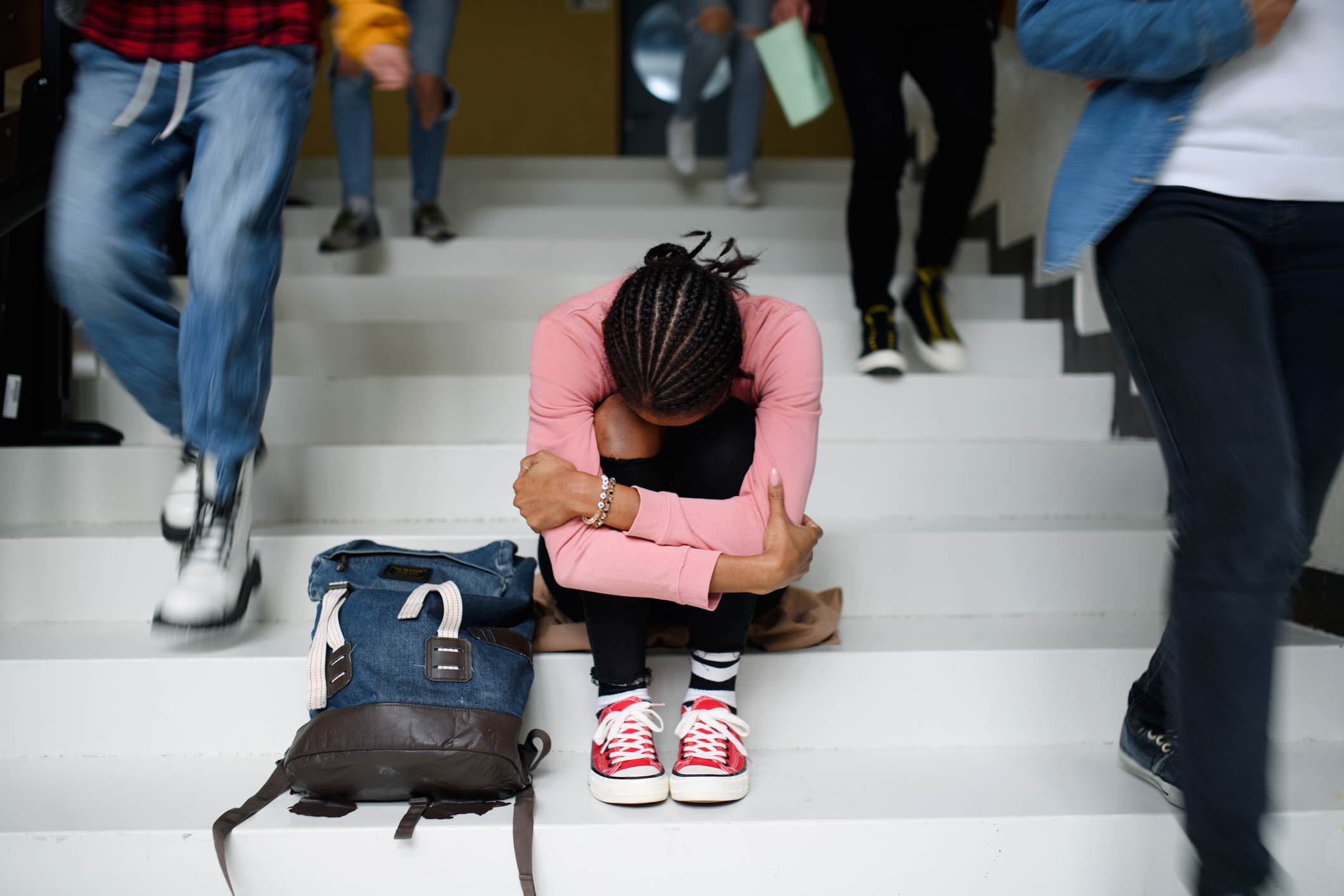 Egy iskolás lány a térdére borulva, egyedül ül az iskola lépcsőjén.