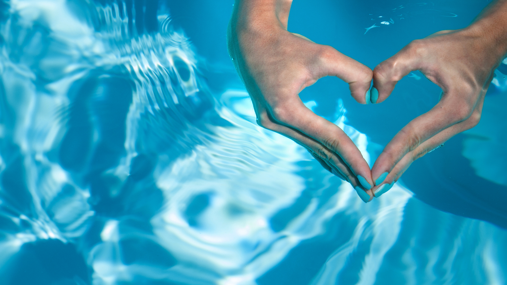 Egy medencében két kéz egy szívet alkot, a lány körmei kékek.