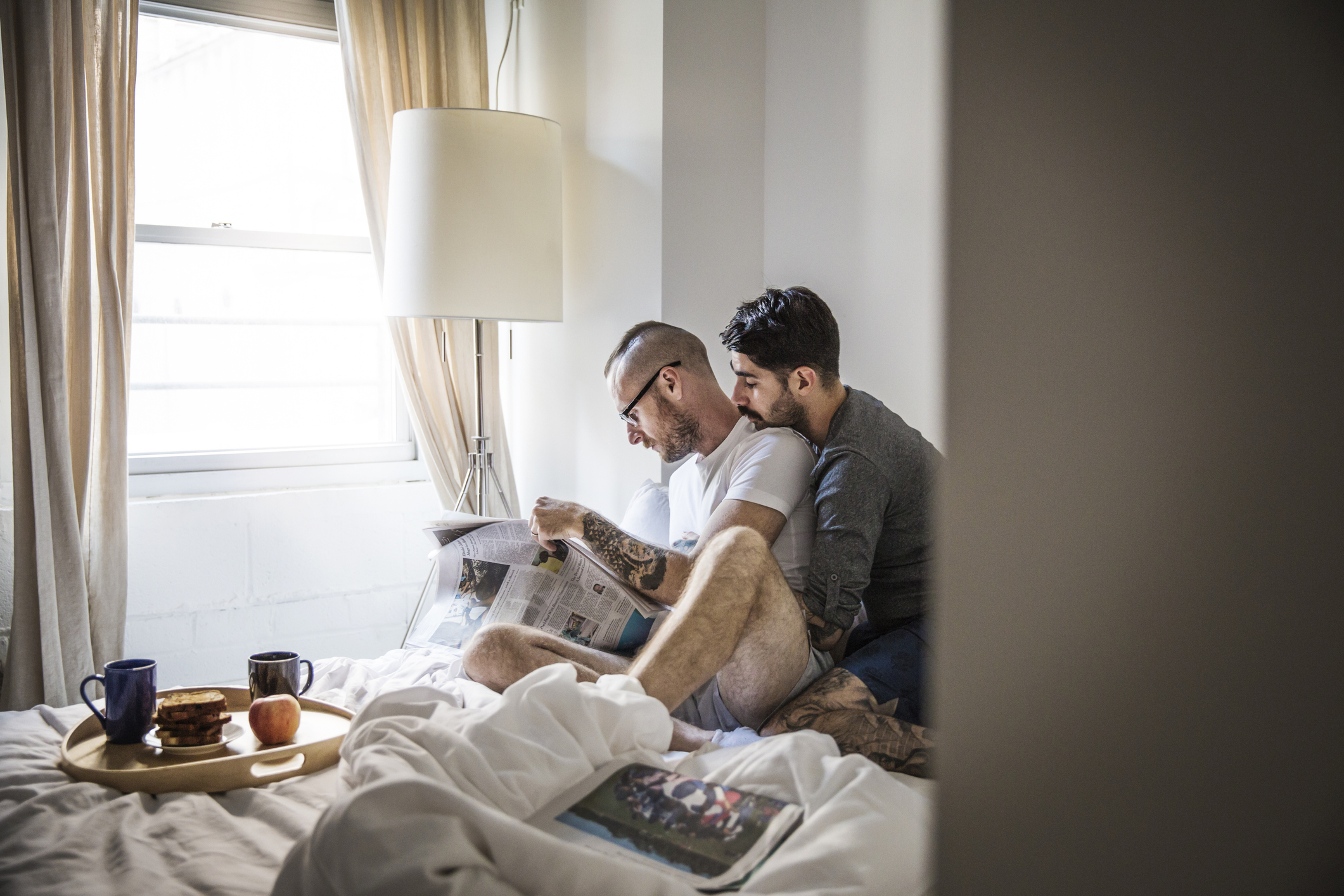 Egy szerelmespár ül az ágyon és a reggeli újságot olvassák, miközben átölelik egymást.
