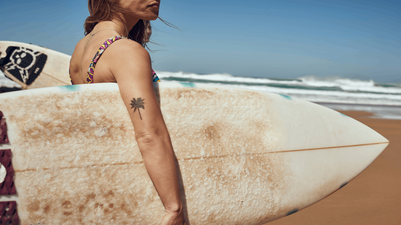 Nő a tengerparton, szörfdeszkával a kezében.