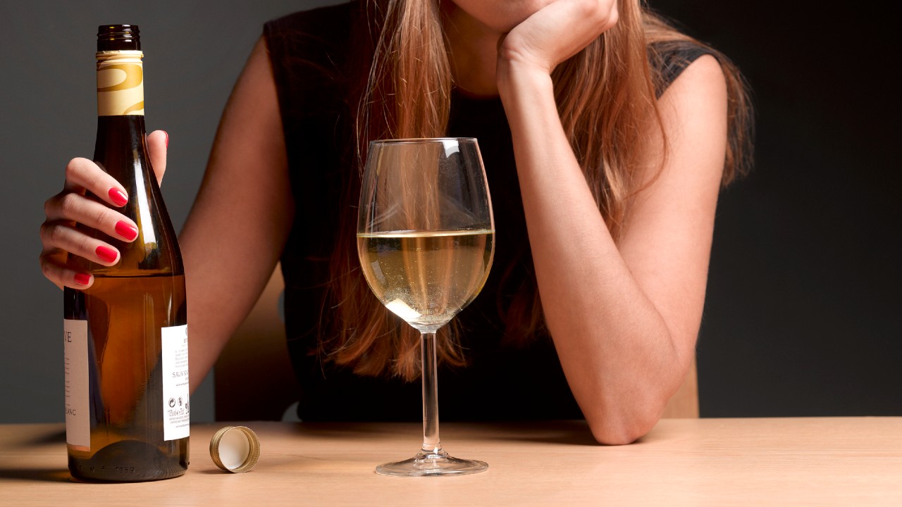 Egy nő ül az asztalnál egy üveg borral.
