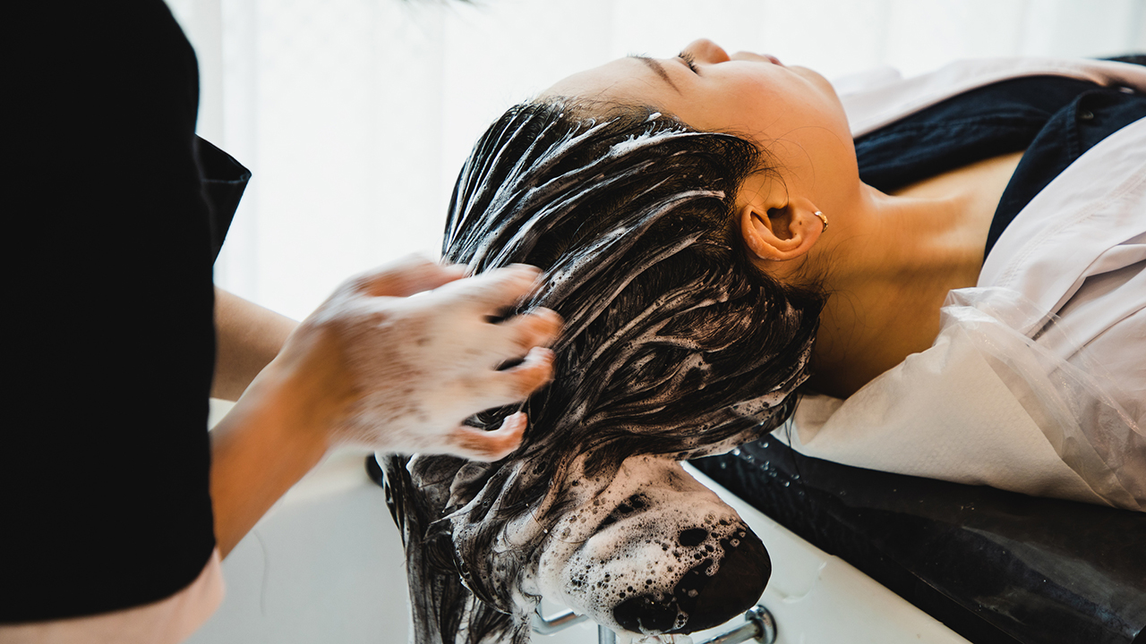 Egy nő ül a fodrászszékben, miközben a fodrász mossa a haját.