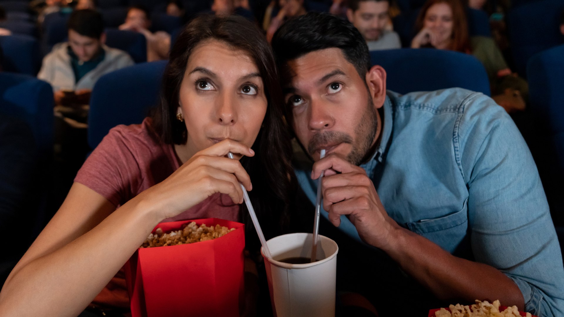 Nő és férfi egy pohárból isznak a moziban.