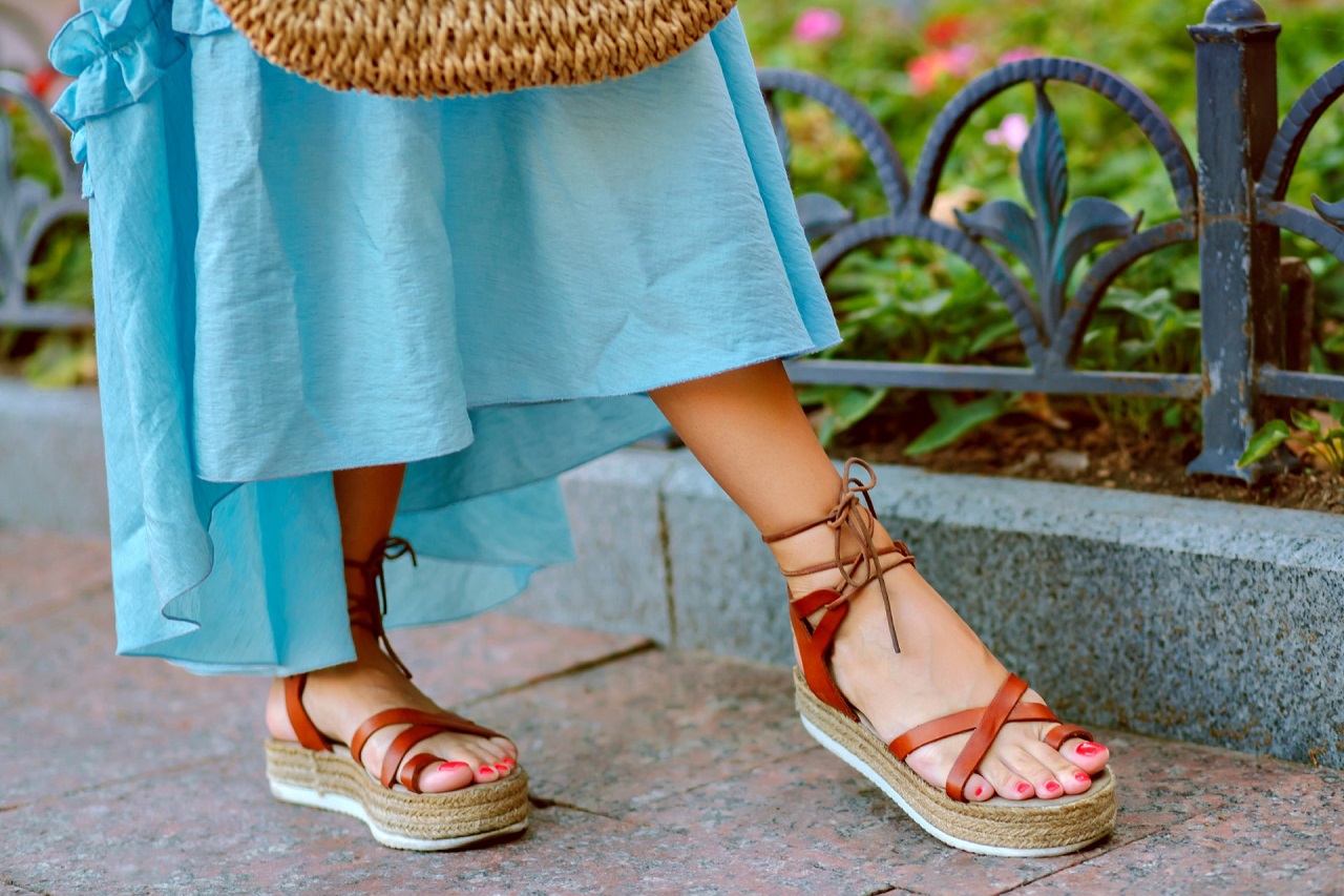 Close up fashion details of woman feet’s, elegant gladiator sandals, blue feminine dress, perfect for summer vacation.