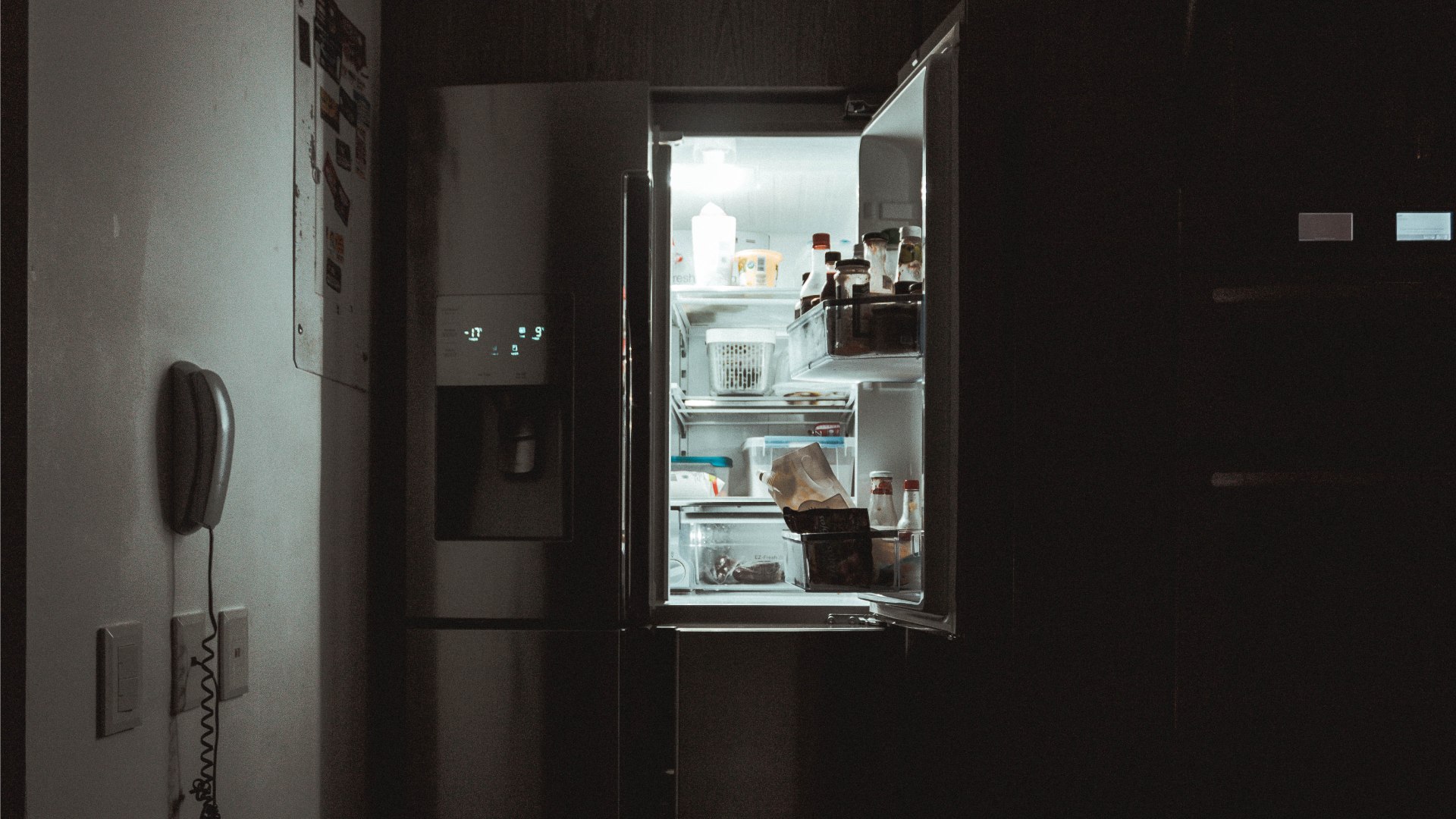 Sötét konyhában nyitott hűtőajtó.