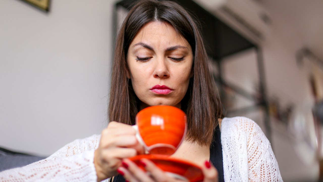 Piros kávéscsészét fintorogva néző nő.