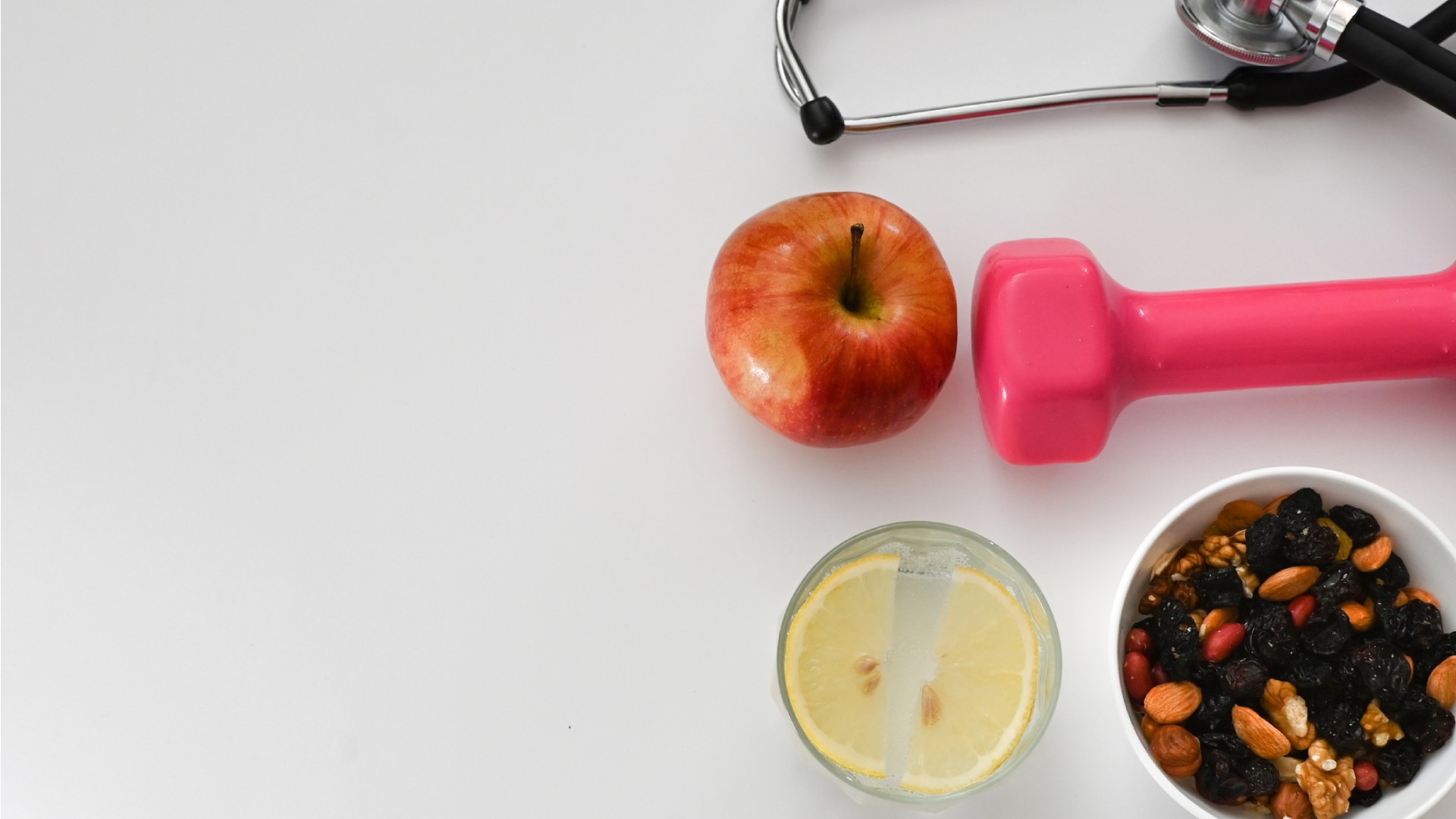 Sztetoszkóp, alma, súlyzó, egy pohár citromos víz, fehér tálkában szárított gyümölcsök és magvak.