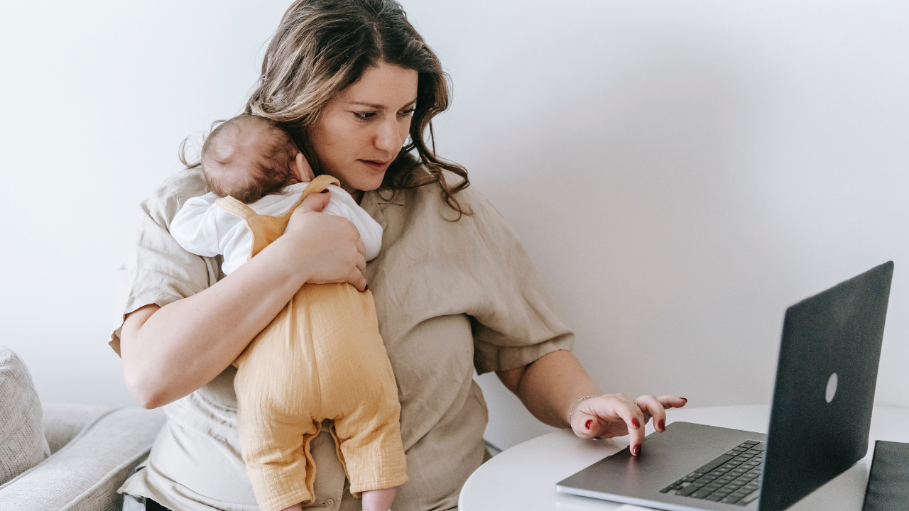 Egy édesanya számítógépezik gyerekkel a kezében