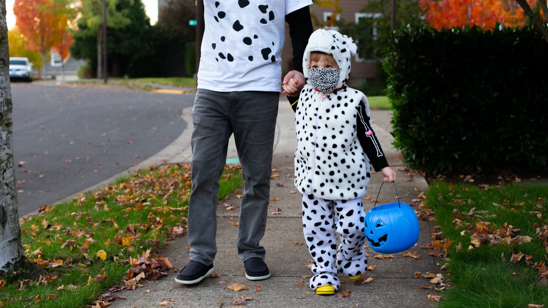Egy apa és lánya jelmezben és kék vödörrel sétál halloweenkor