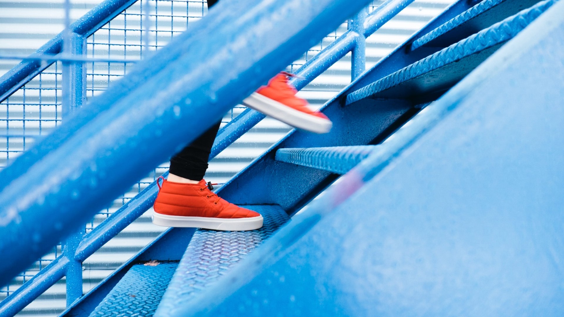 Kék lépcsőn narancssárga cipőben felmenő ember.