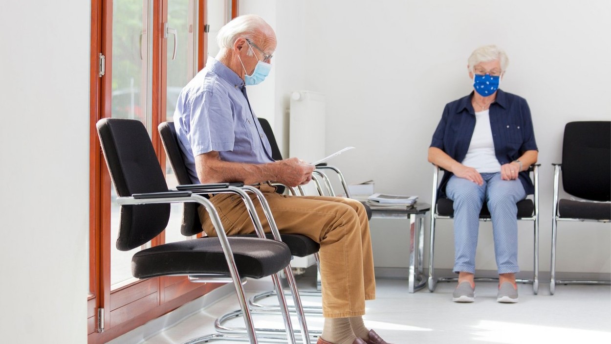 Idős emberek ülnek egy orvos váróteremben szájmaszkban