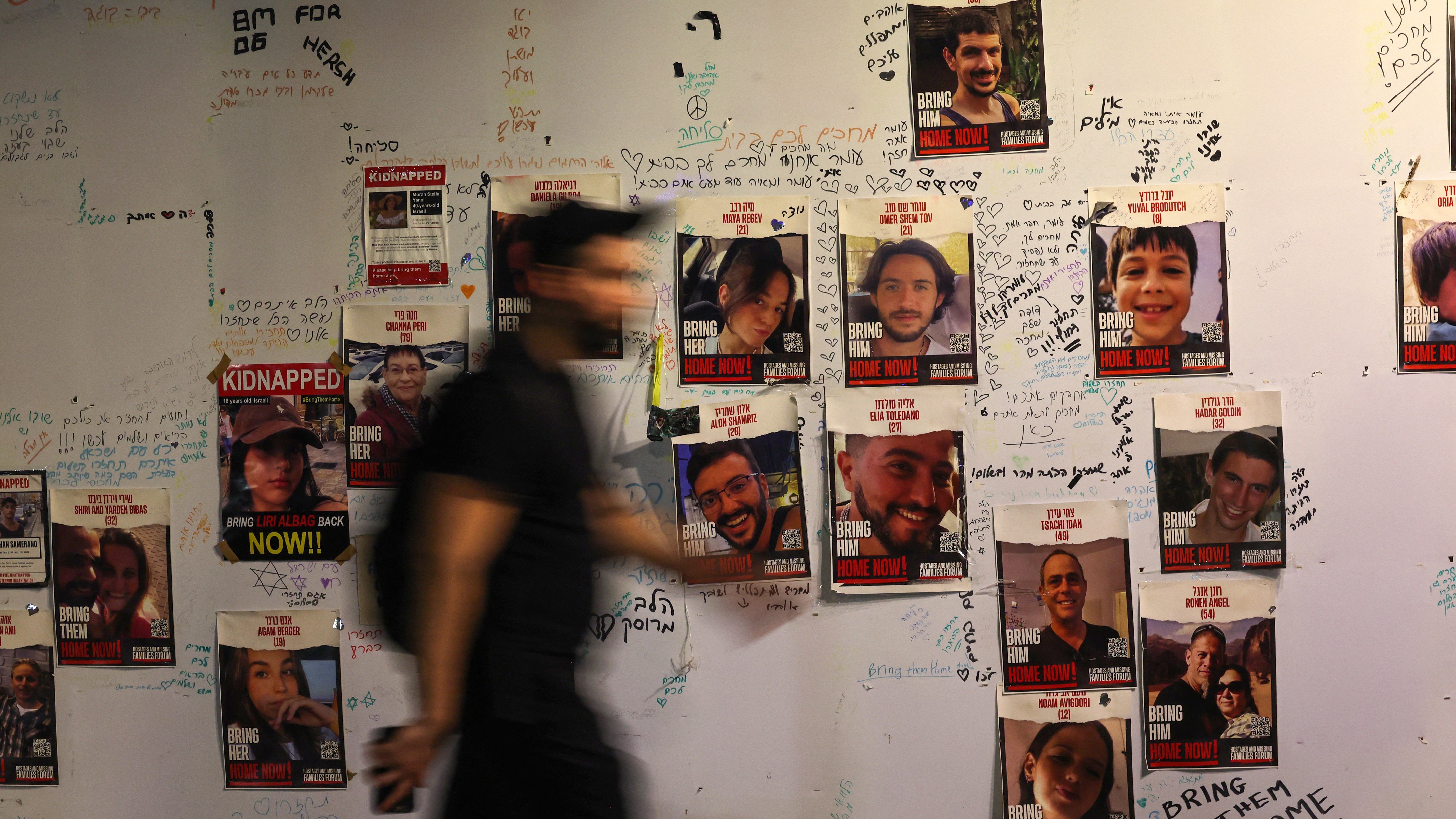 Egy férfi sétál az izraeli túszok falra kifüggesztett portréi mellett Tel-Avivban