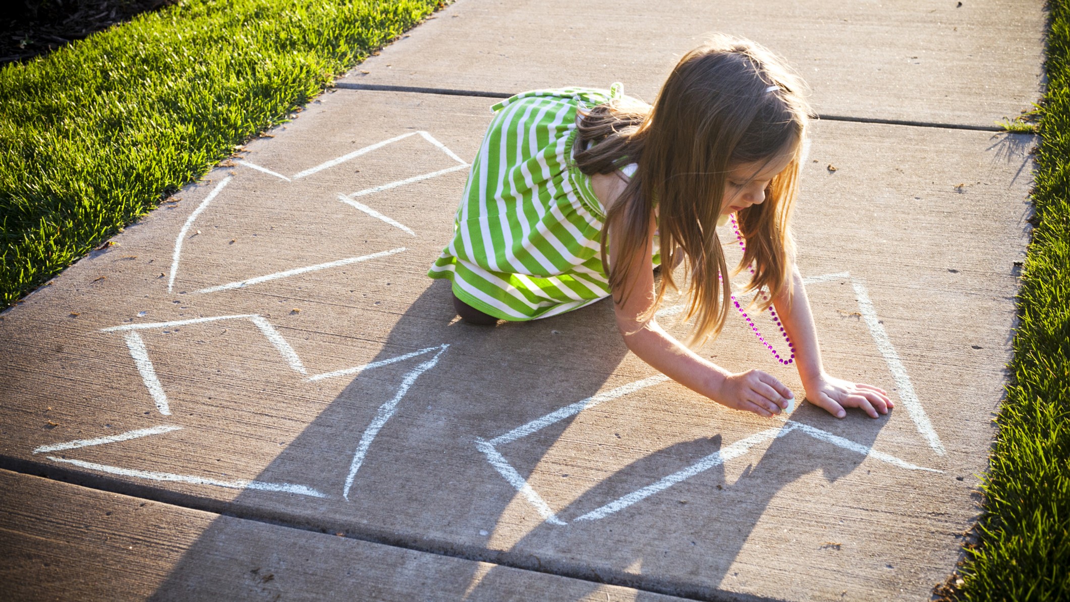 Kislány krétával rajzol a járdára