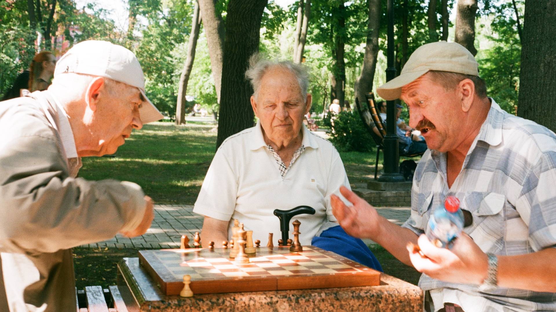 Három idős úr sakkozik a parkban.