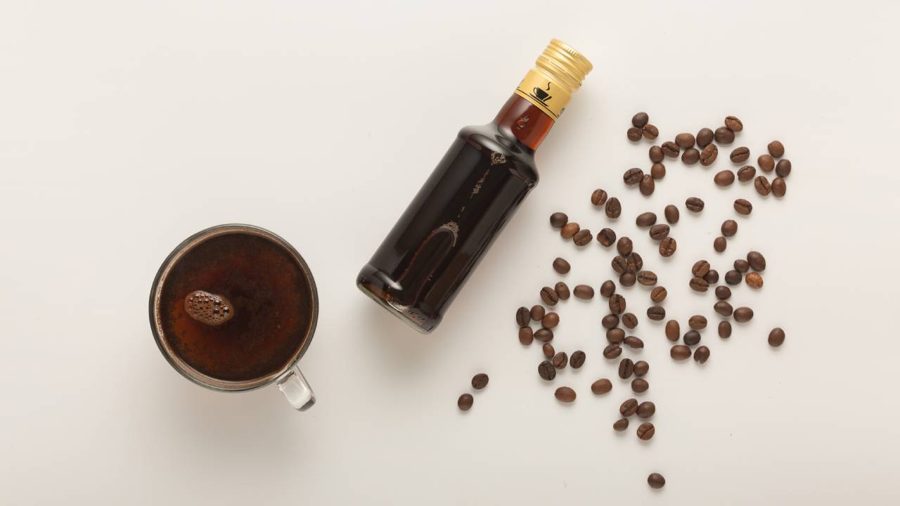 Egy csésze kávé, kávélikőr és kiszórt kávészemek.
