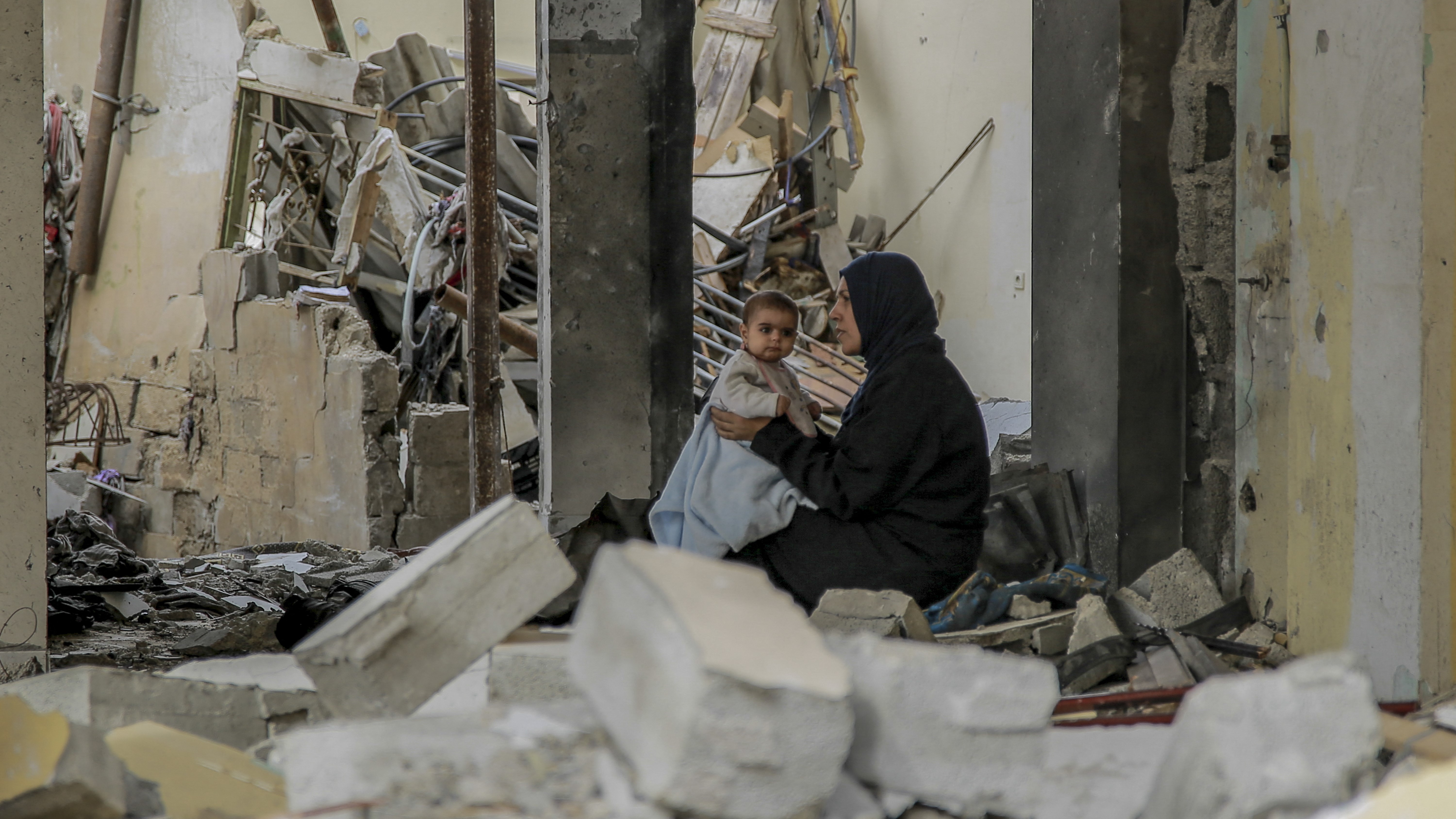 Egy palesztin nő tartja kisbabáját a lerombolt épületek romjai között Gáza városában 2023. november 25-én