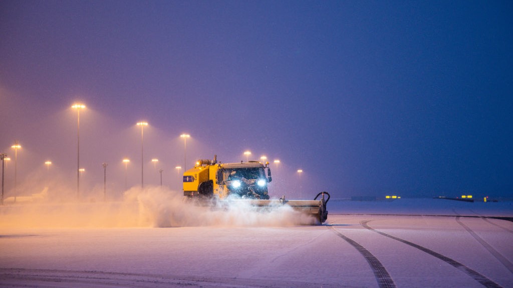Egy hókotró tisztítja a kifutópályát a pekingi nemzetközi repülőtéren a havazás után 2023. december 11-én