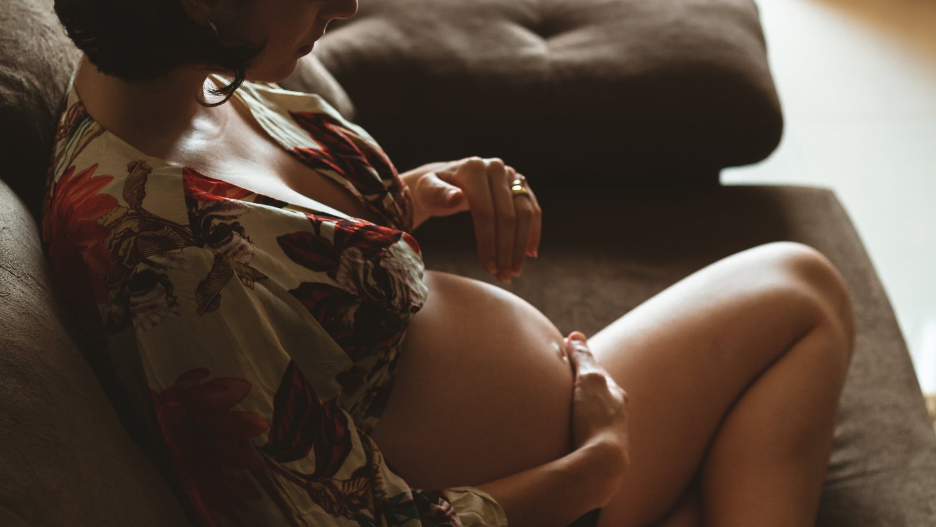 Terhes nő fogja a csupasz hasát a kanapén ülve