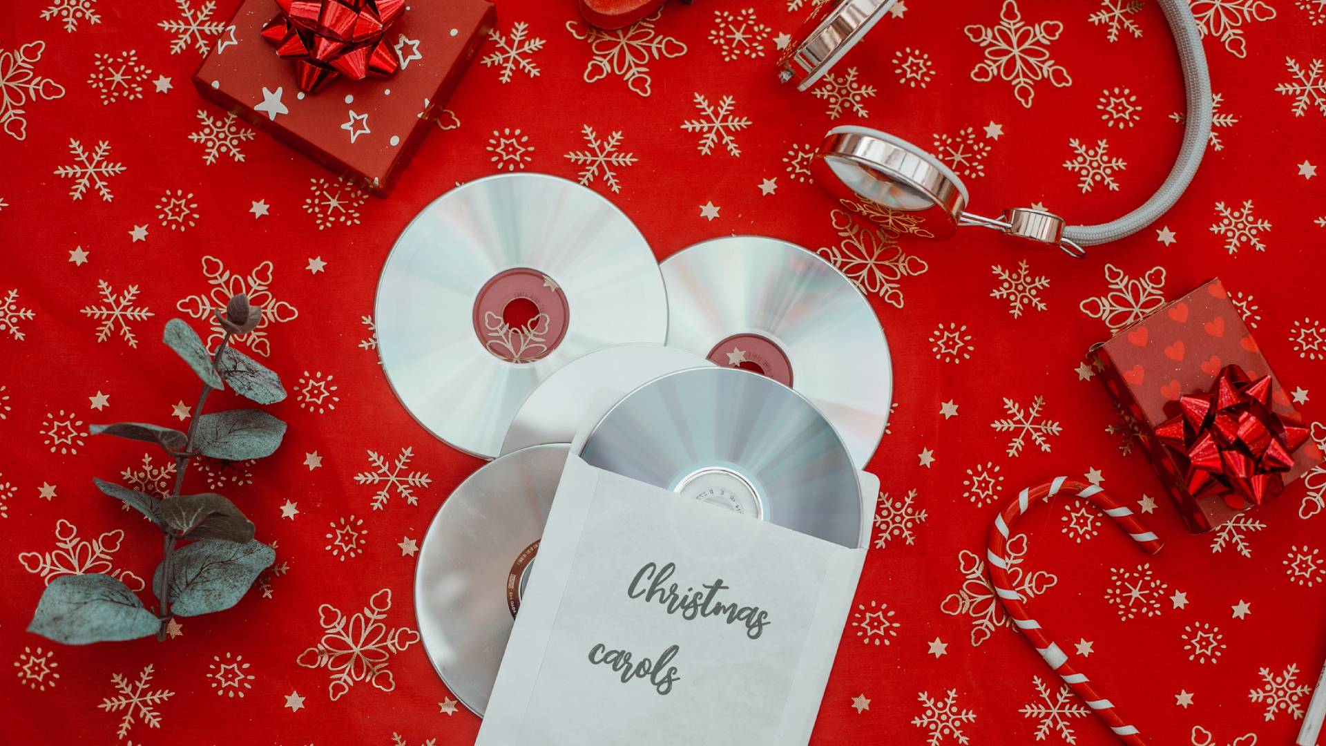 Piros terítőn CD karácsonyi dalokkal, ajándékkal, cukorrúddal és fejhallgatóval.