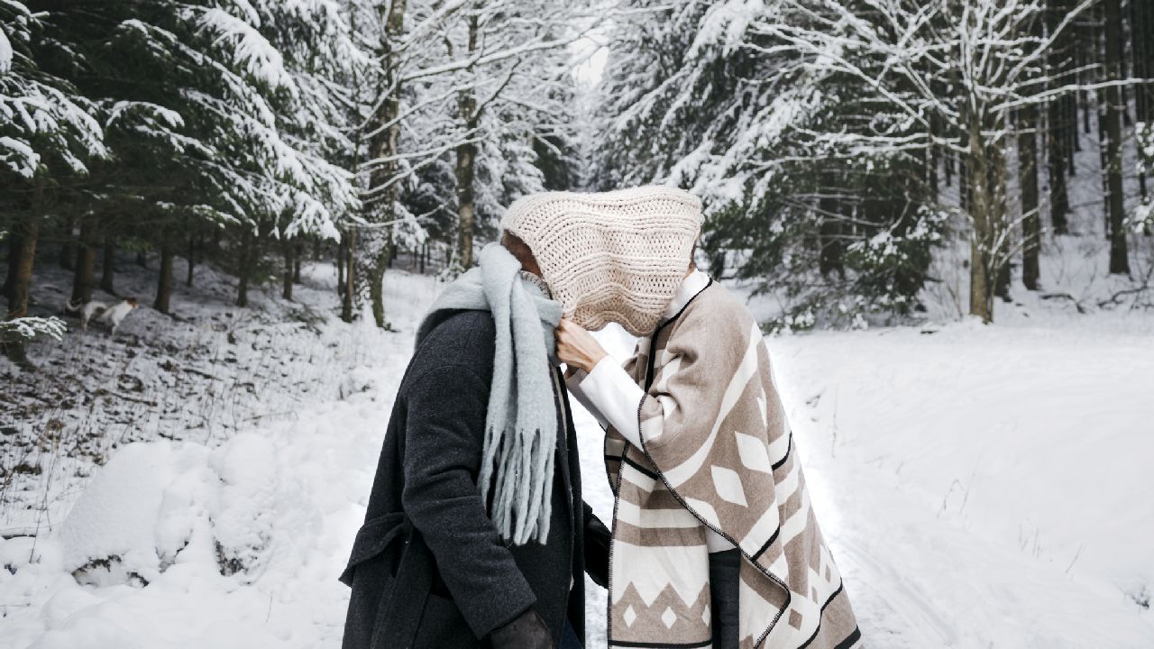 Szerelmespár közös sálban összenézve a havas erdőben