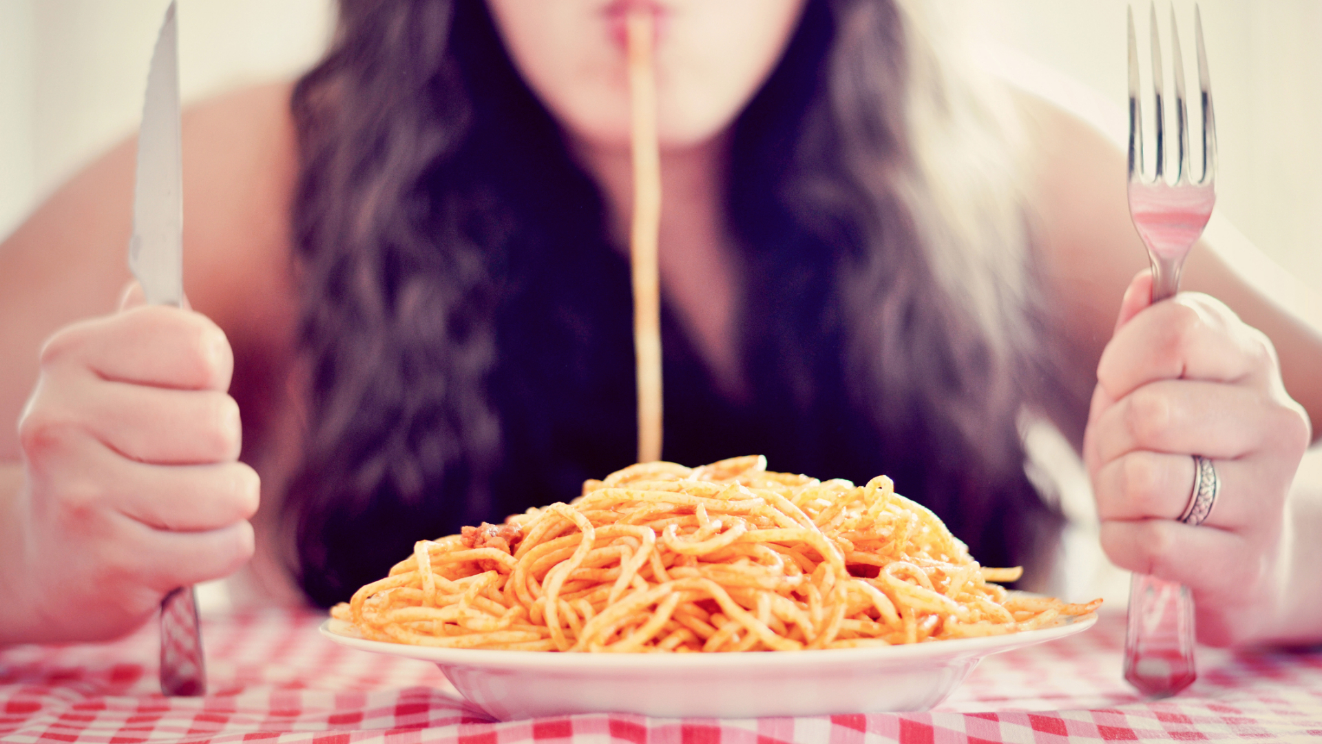 Spagetti lóg egy nő szájából, felfelé mutató evőeszközök a kezeiben