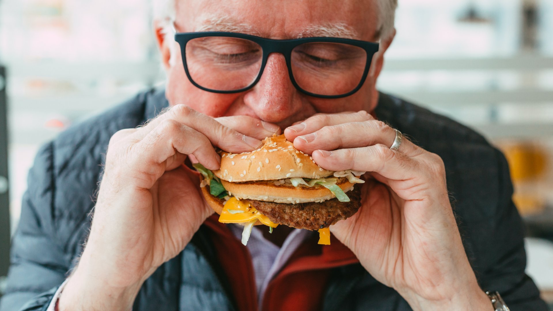 Egy idős szemüveges férfi hamburgert eszik