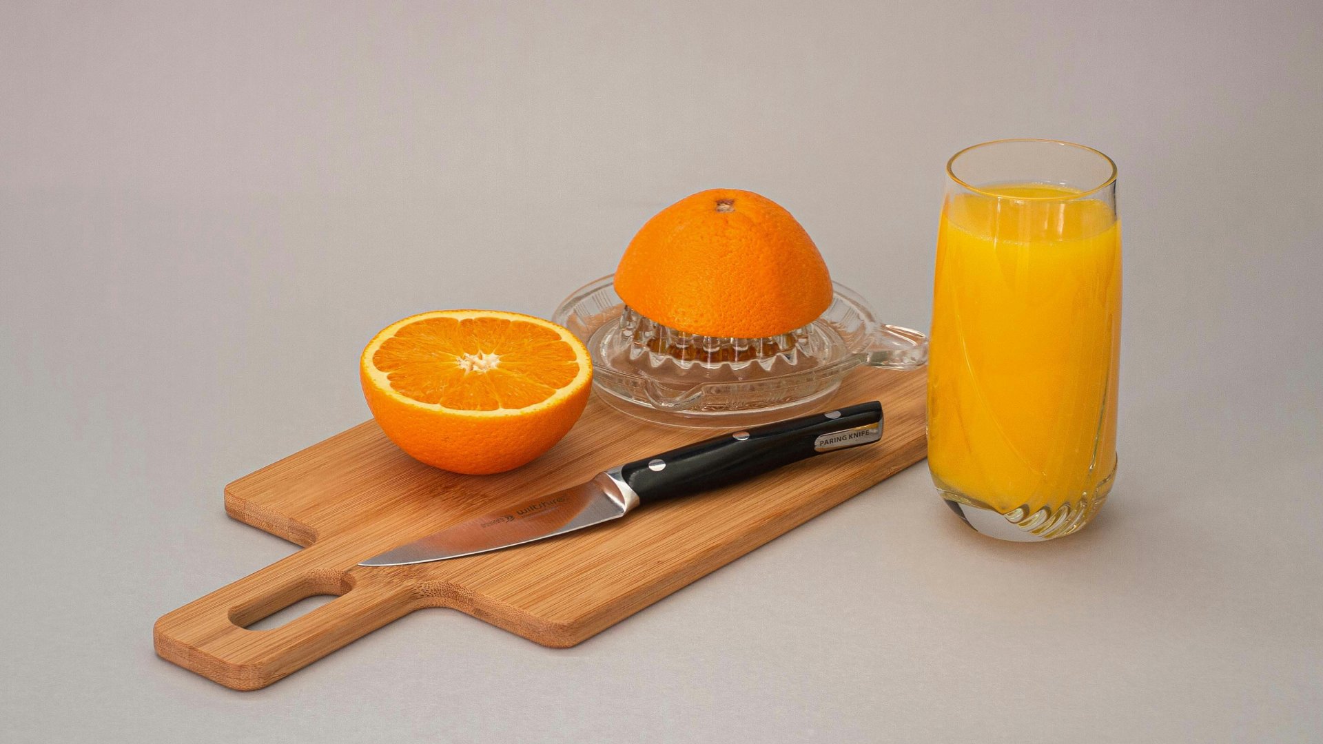 Kifacsart narancslé, facsaró, kés, vágódeszka és egy félbe vágott narancs.