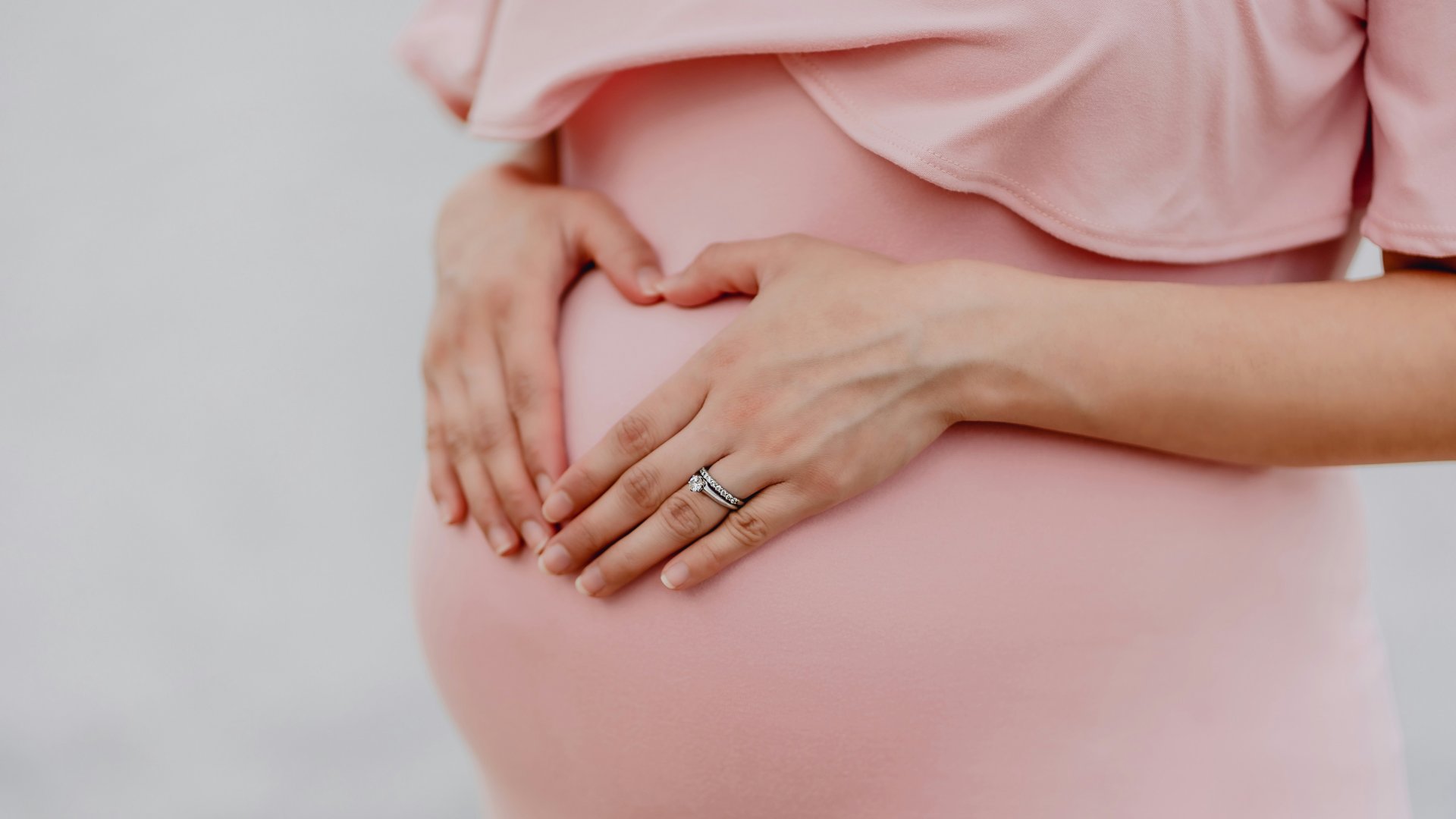 Egy terhes nő szívet formál a kezével a hasán