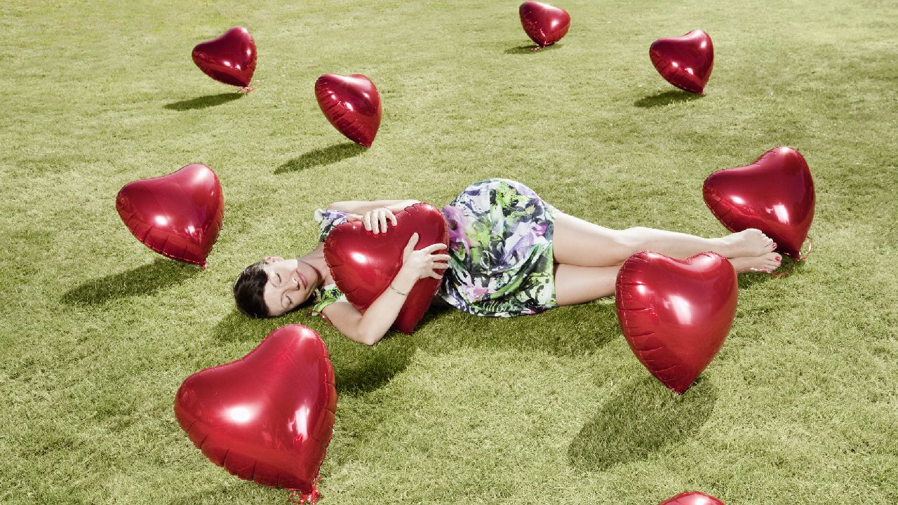 Lány fekszik a fűben piros szív-lufikkal