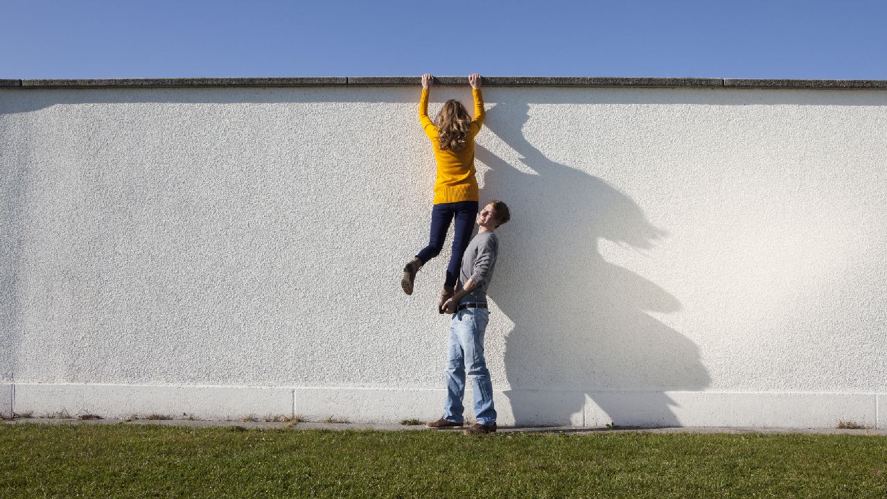 Falon átmászó nőt segít egy férfi