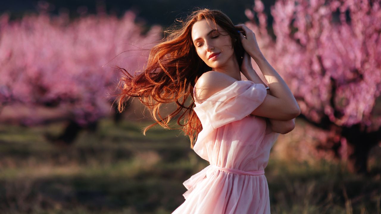Hölgy rózsaszín ruhában virágzó fák előtt