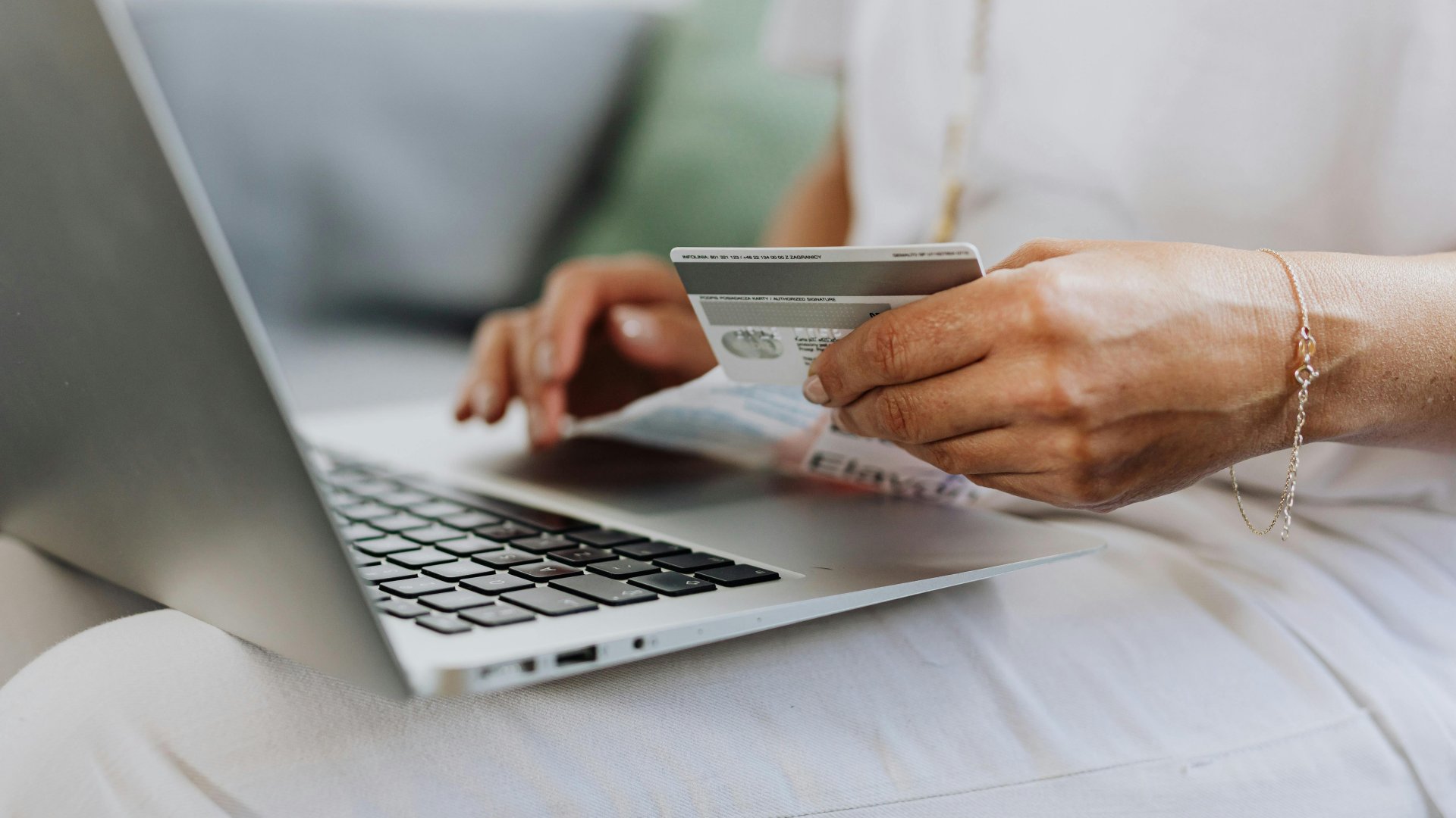 Egy nő bankkártyával vásárol a neten, ölében laptoppal