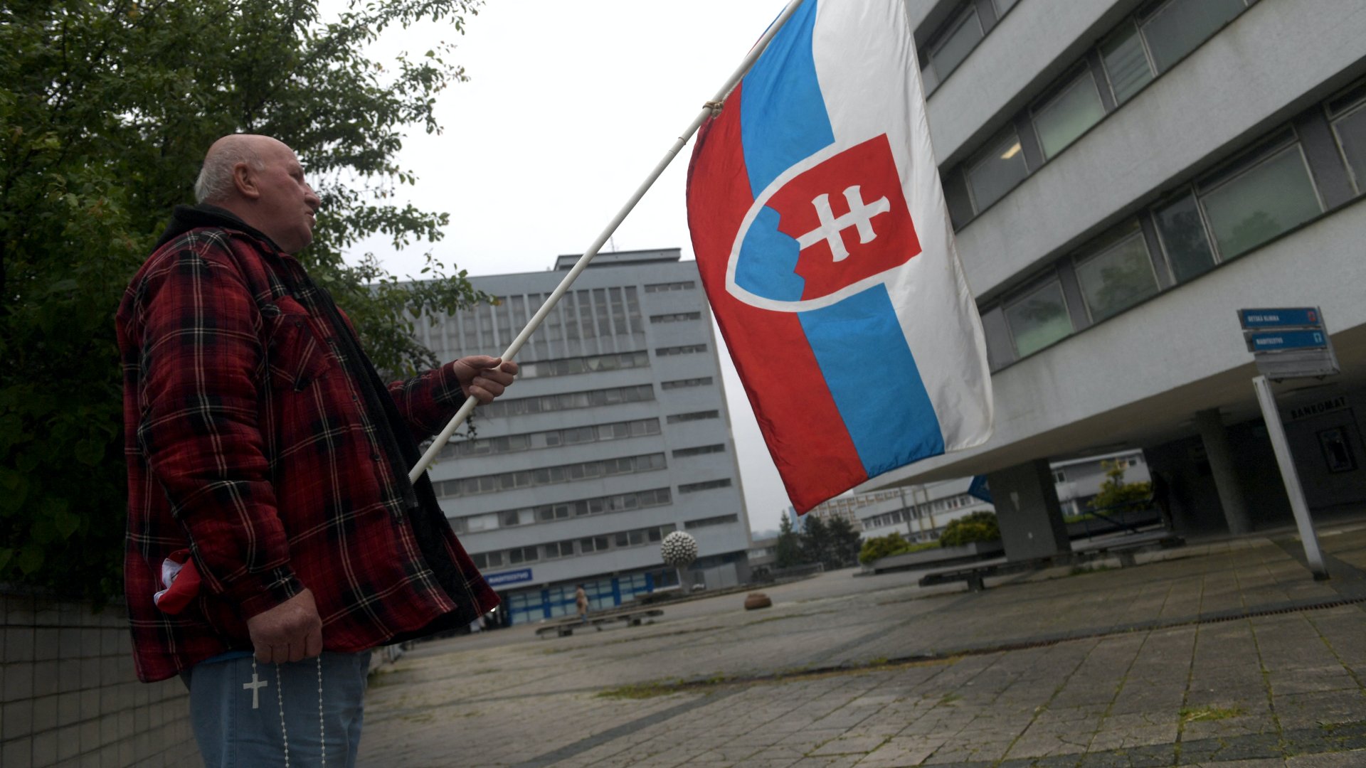 A szlovák kormány egyik támogatója egy szlovák zászlót tart a kezében 2024. május 17-én a besztercebányai kórház előtt, ahol Robert Fico szlovák miniszterelnököt kezelik