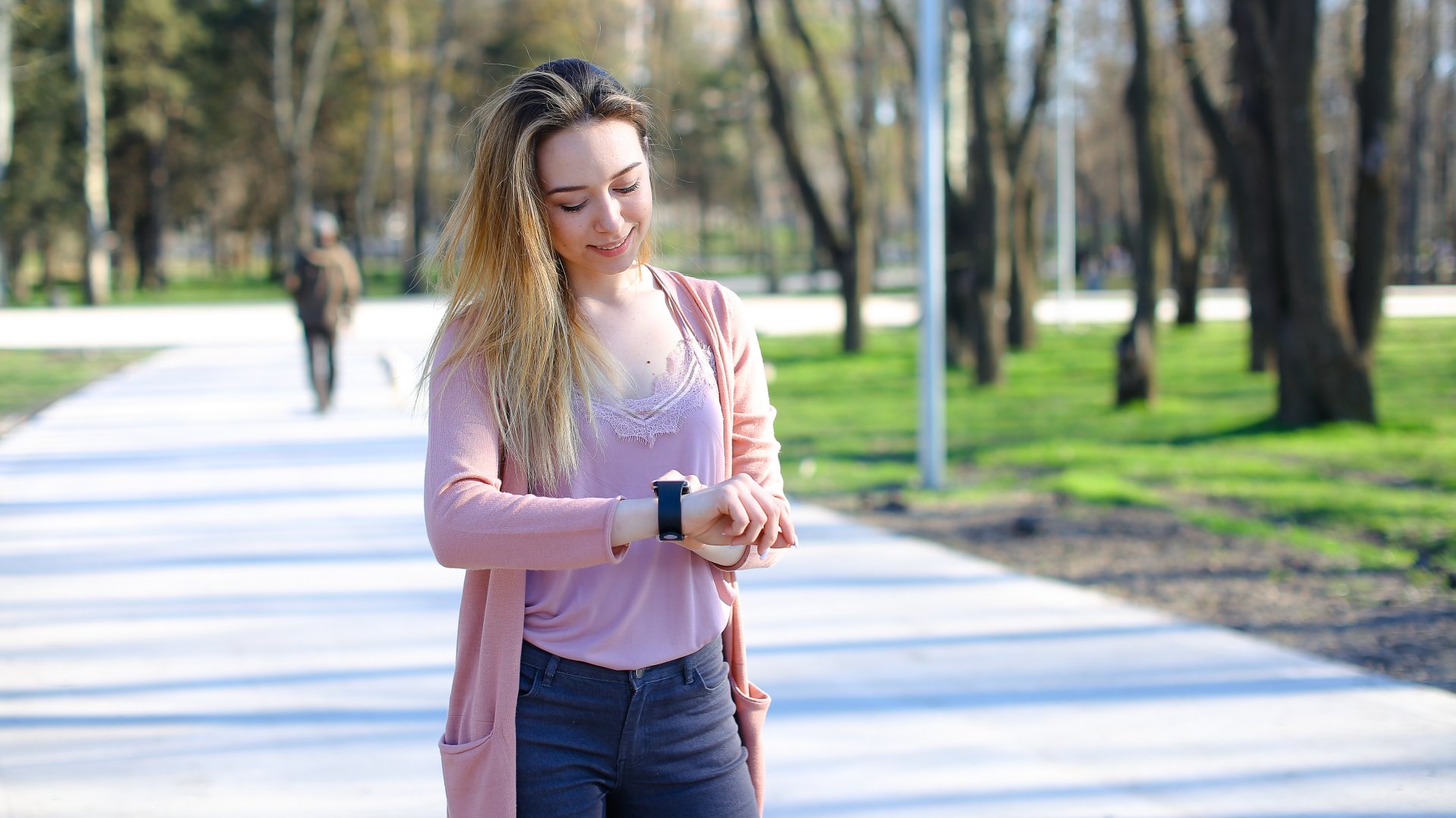 Egy fiatal nő az okosóráját nézi a parkban séta közben