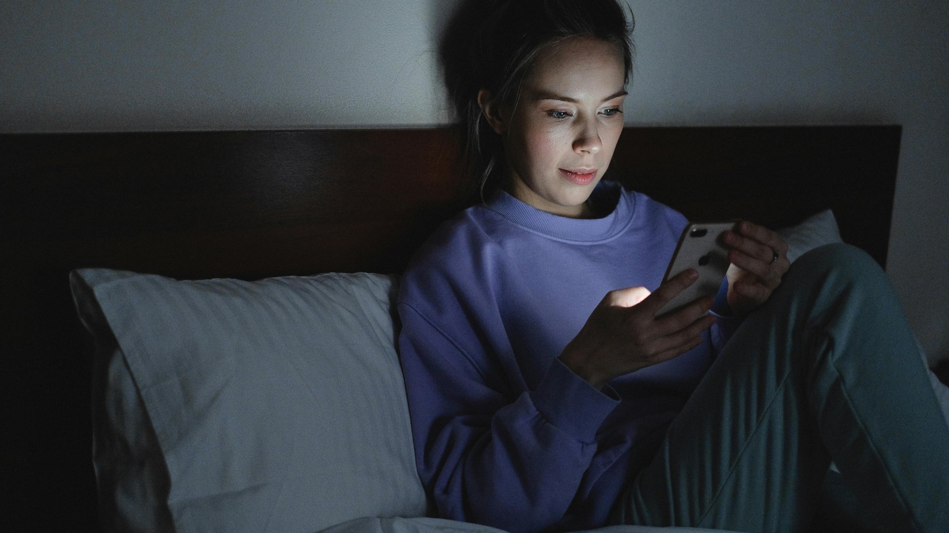 Egy fiatal nő telefonozik az ágyban este