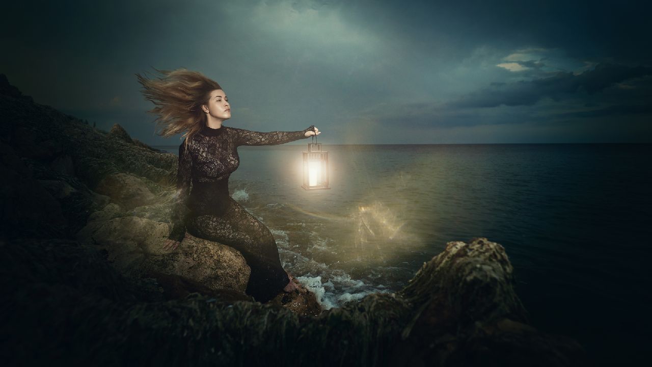 Nő lámpással a tengerparti sziklákon