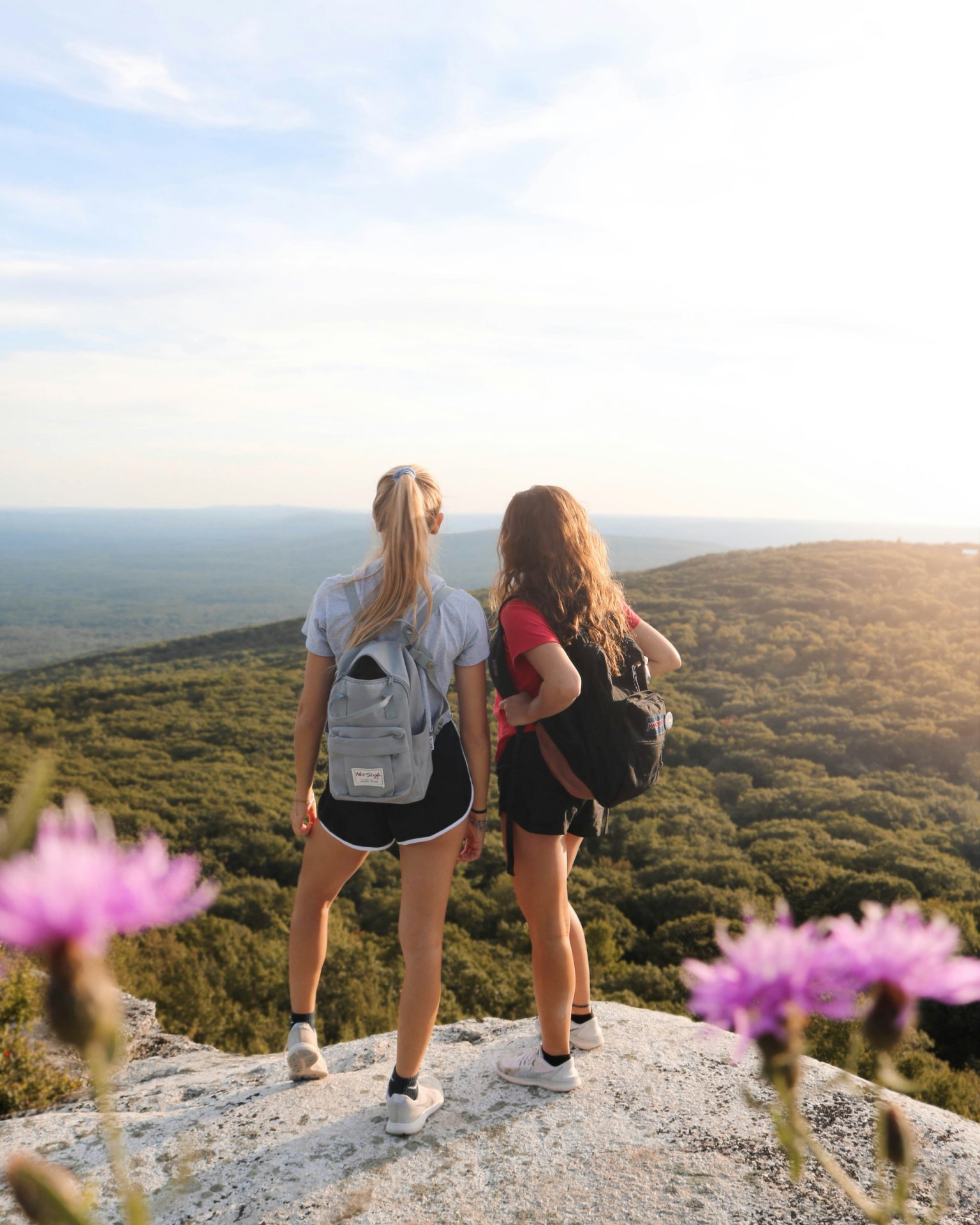 Két fiatal nő nézi a tájat egy dombtetőről