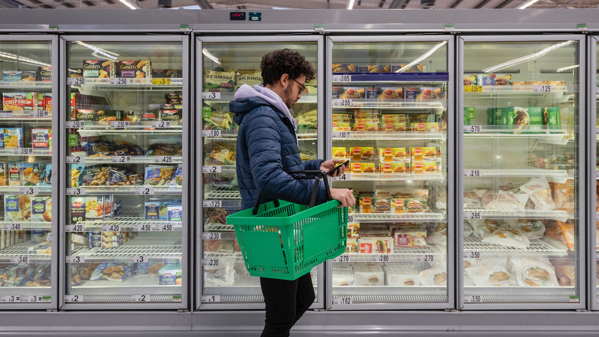 Egy férfi a telefonját nézi egy szupermarket hűtője előtt