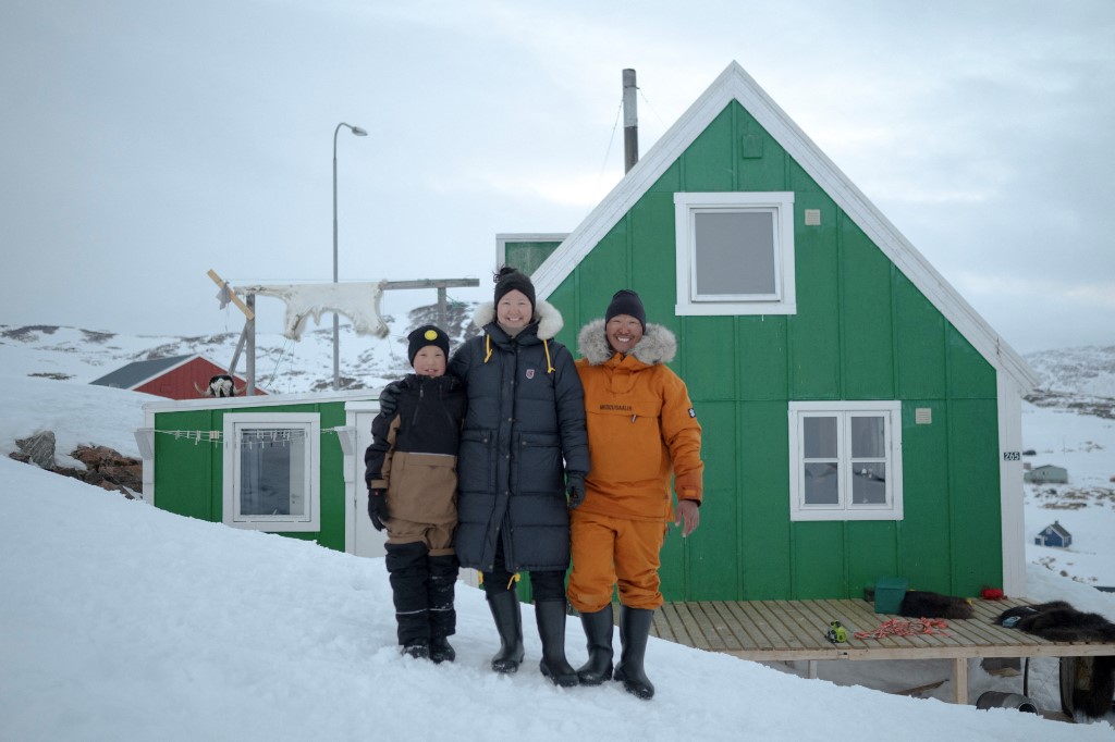 Martin Madsen, egy 28 éves hivatásos inuit vadász, feleségével, a 40 éves Charlotte Pike-kal, és 8 éves fiukkal, Noah-val pózol házuk előtt Ittoqqortoormiiten, a Scoresbysund-fjord jegén 2024. április 30-án. Ittoqqortoormiit falu, színes házaival és 350 lakosával, a világ legnagyobb fjordjának, a Scoresby-szorosnak közelében található, Grönland keleti partján, az Arktisz peremén. A falu összes férfija vadász – a hivatásosak jegesmedvékre vadásznak, az amatőrök fókákra, narválokra vagy pézsmatulkokra. Ez egy ősi életmód, amely generációról generációra öröklődik.Az elmúlt húsz évben azonban az éghajlatváltozás és a kvóták fokozatosan veszélyeztették ezt a hagyományt, amely az inuit családok túlélését biztosítja.